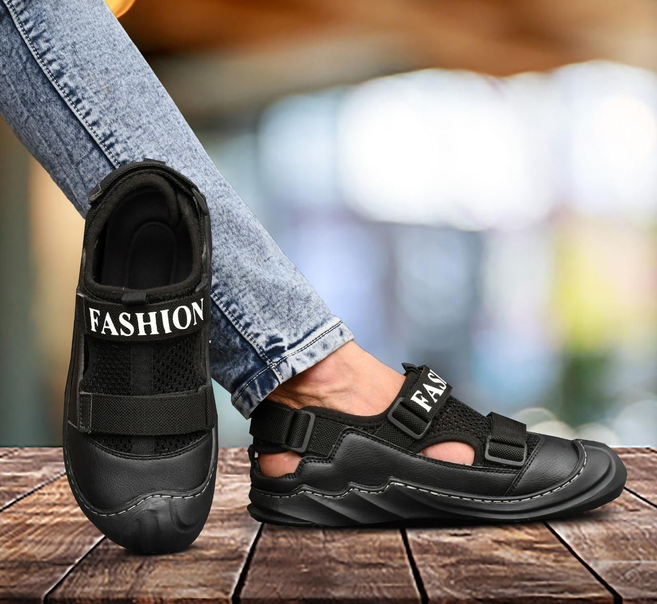 Black sandals with 'FASHION' text worn by a person on a wooden surface.